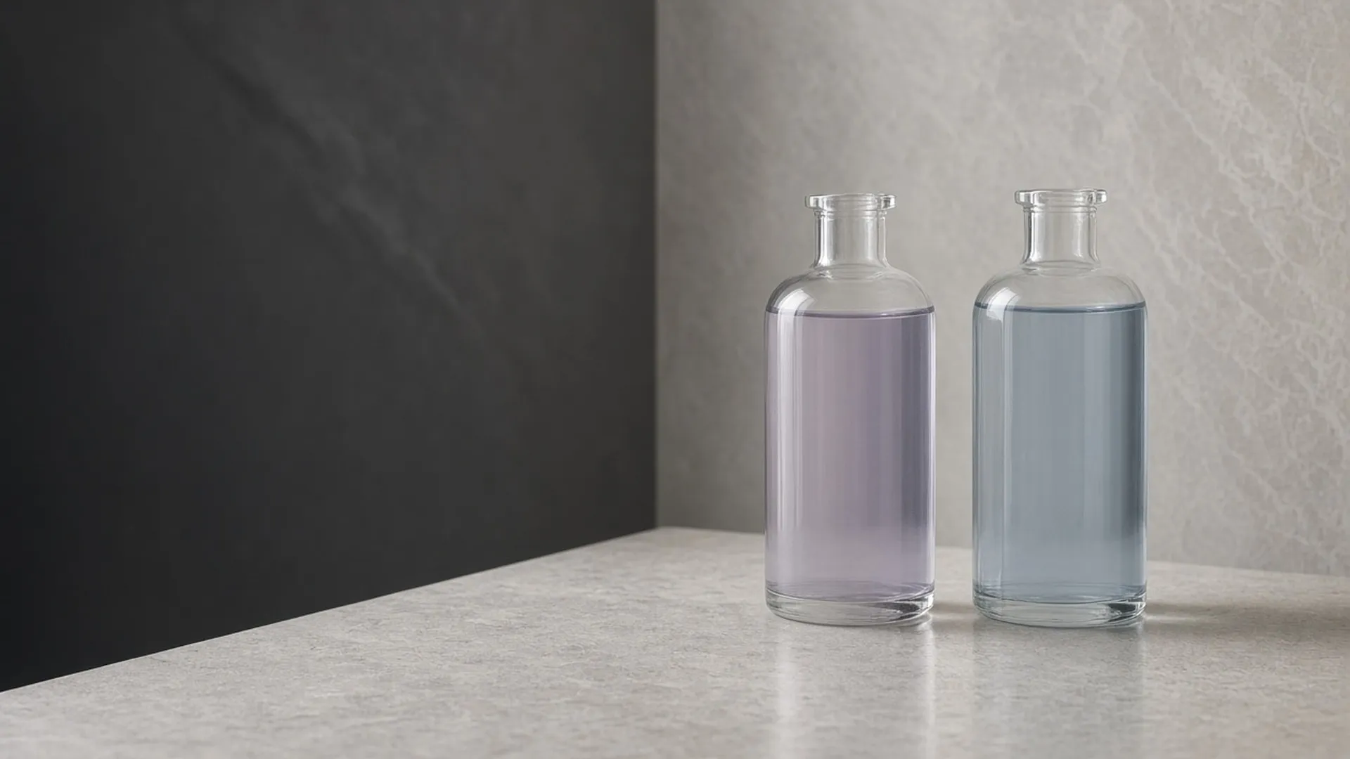 Two clear unlabeled glass bottles holding pale lilac and pale blue liquid on pale stone