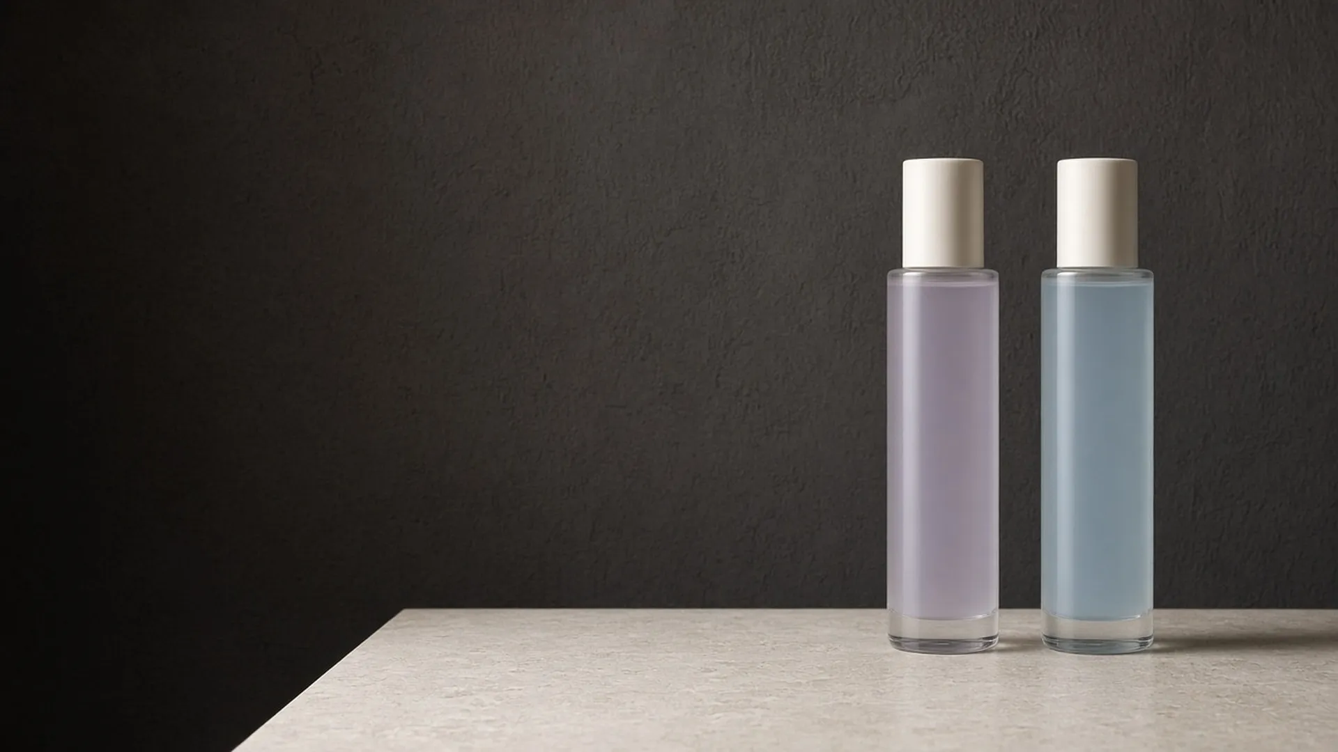 Two clear unlabeled glass bottles with white caps holding pale lilac and pale blue liquid