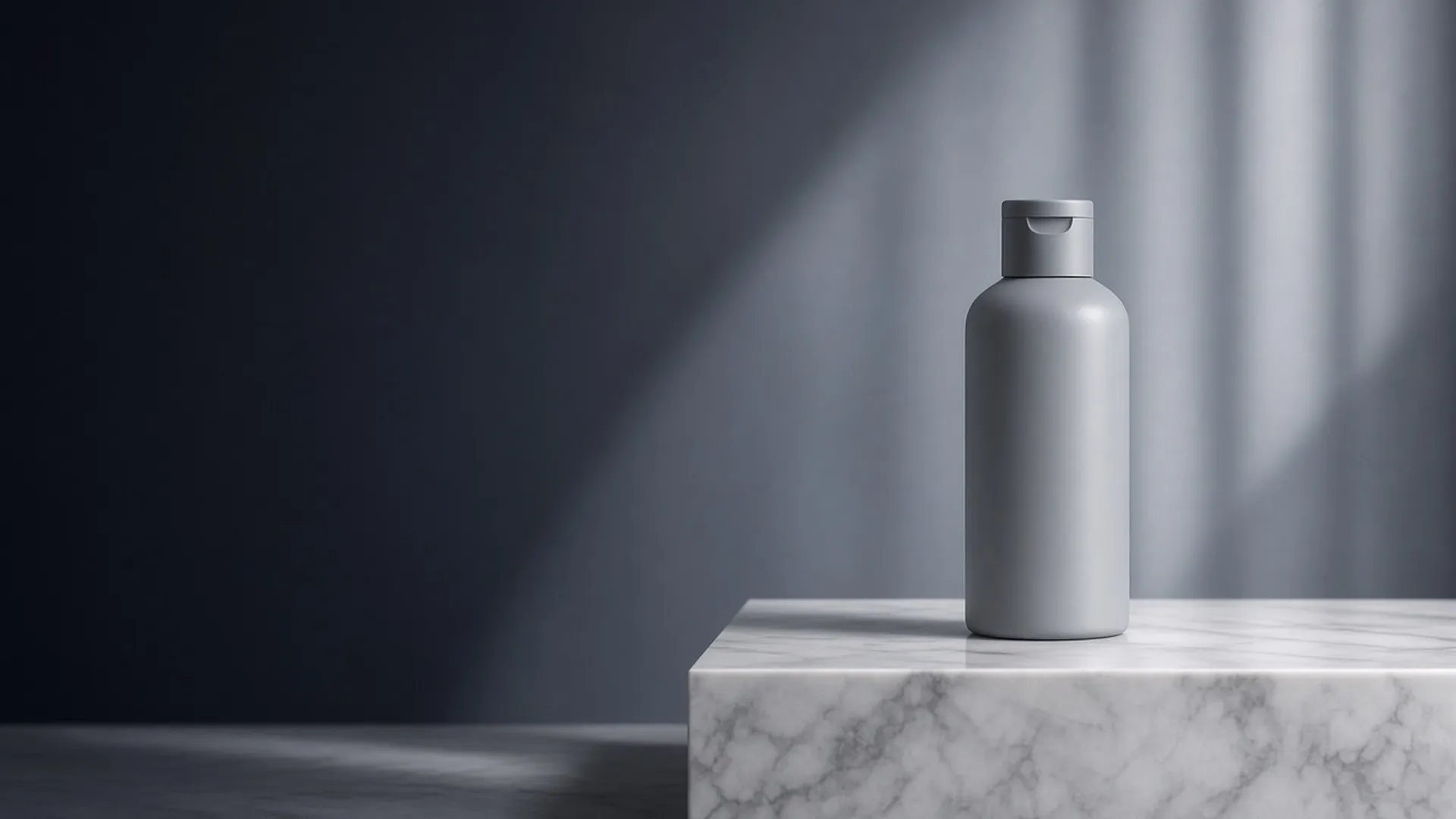A plain pale grey bottle with a flip cap standing on a white marble ledge