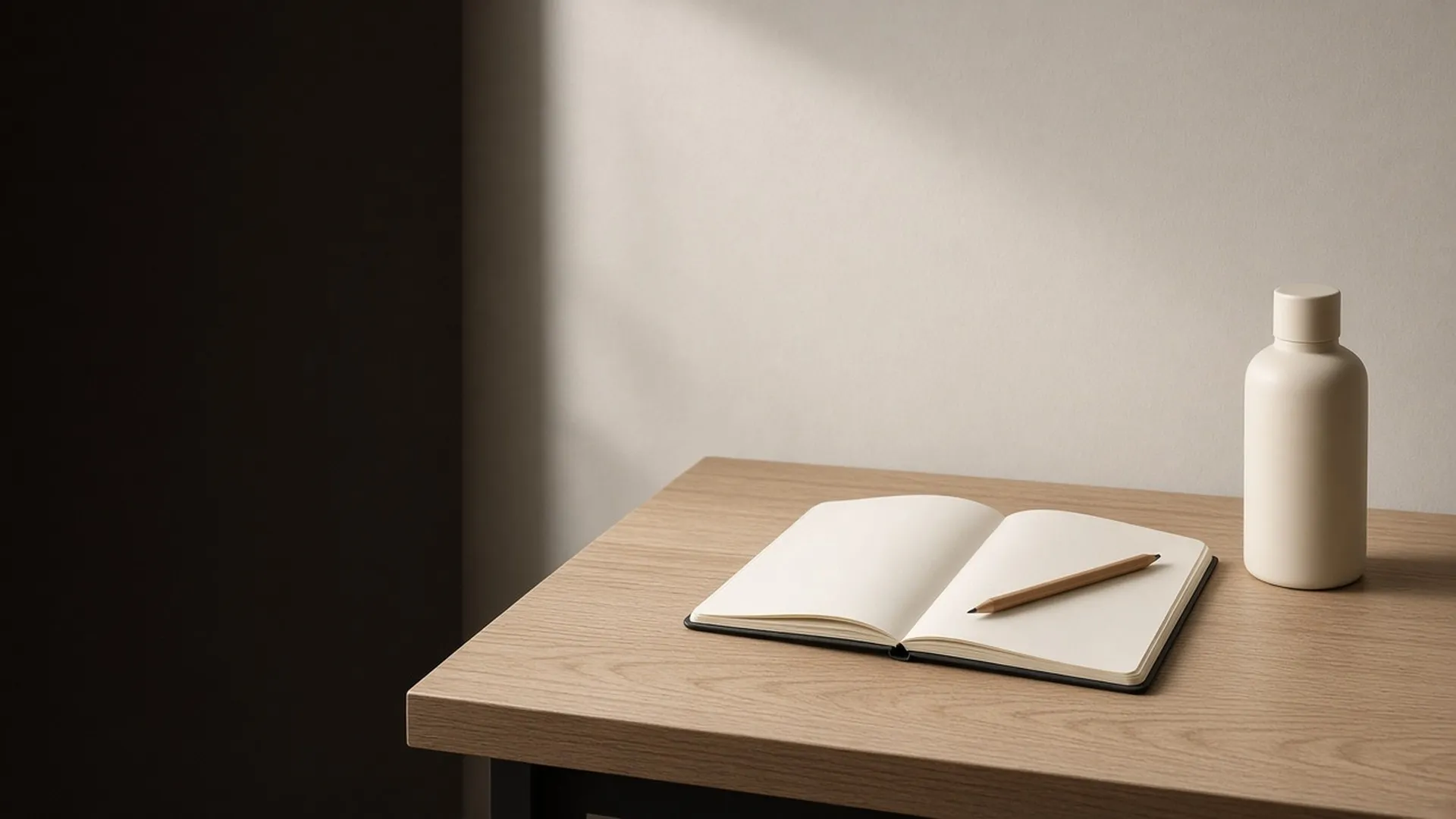 An open blank notebook and a pencil on an oak desk beside a plain bottle